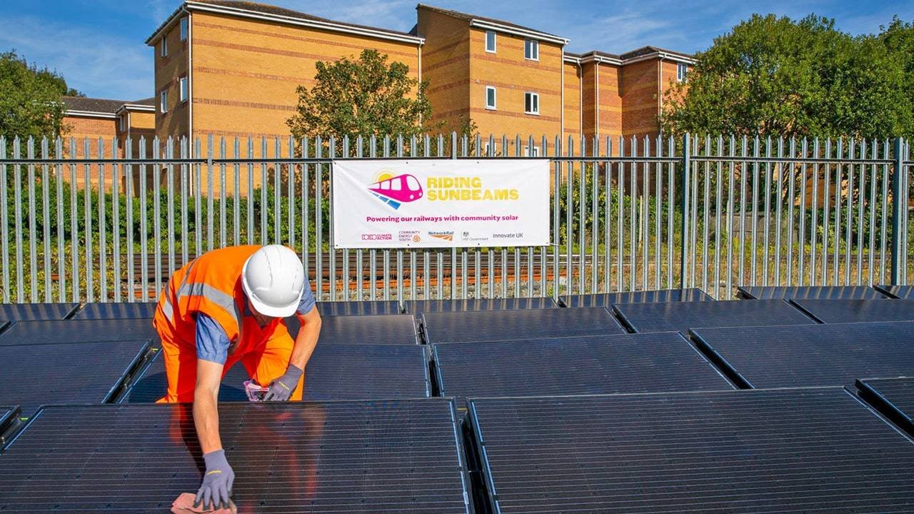 İngiltere'de demiryolu kenarına kurulan güneş panellerinde çalışan teknisyen, arkada Riding Sunbeams pankartı